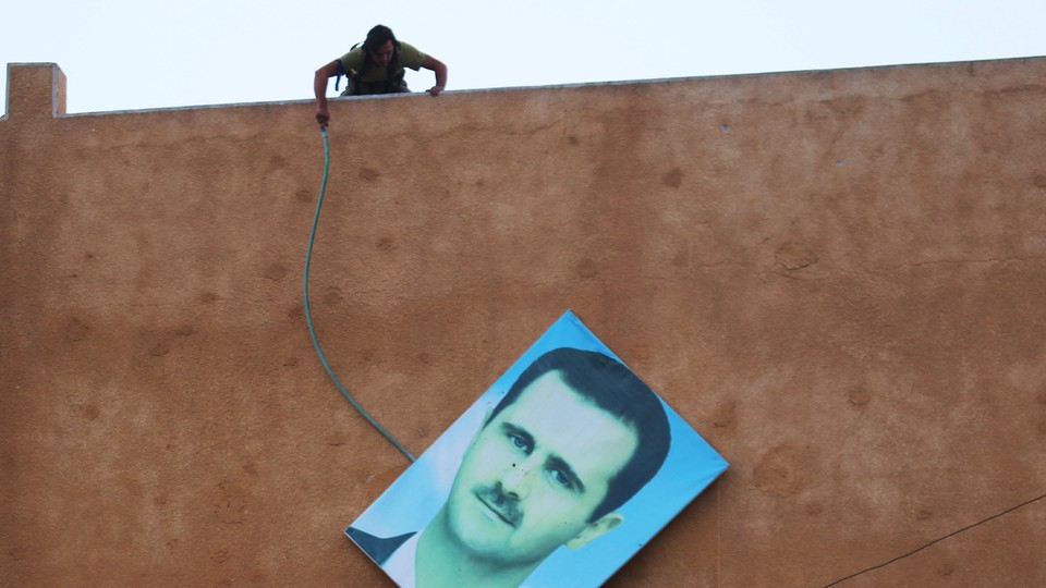 A rebel fighter stands atop a building and takes down a large picture of Assad after rebels captured the area in 2015.