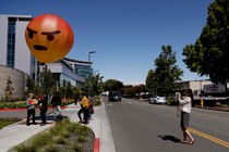 People hold a balloon version of the "angry" emoji.