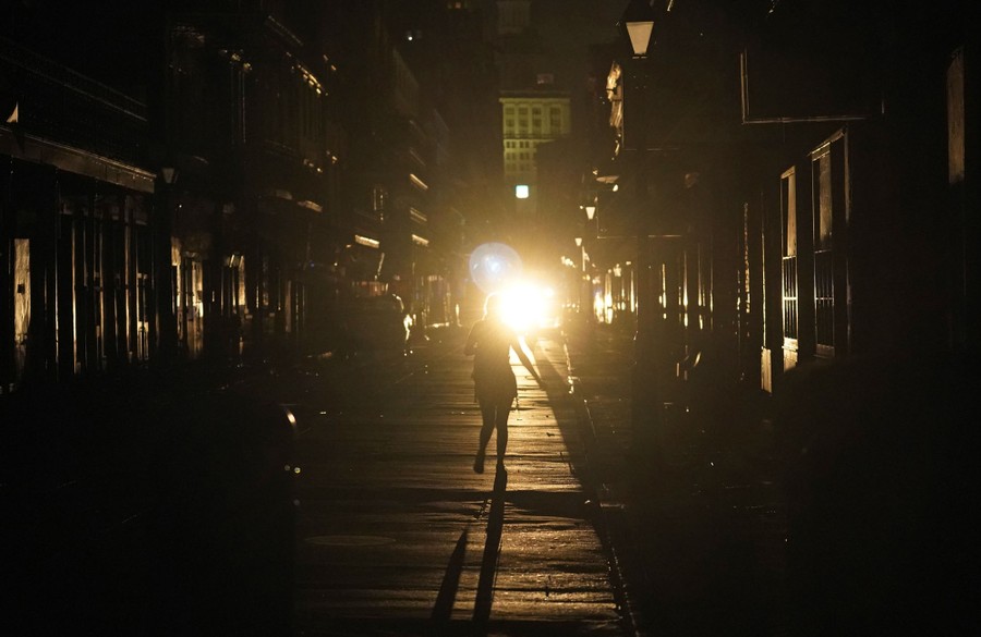 Woman walks down a darkened street at night toward a single bright light.