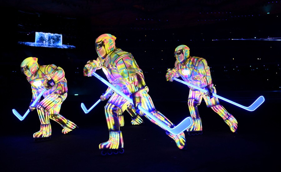 Performers wearing glowing hockey-player costumes skate across a stadium floor.