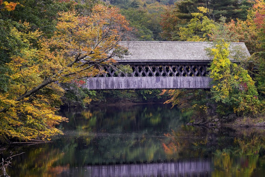 A covered bridge above still water, surrounded by trees with fall colors