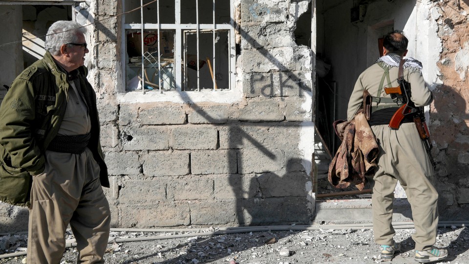 A color image of two members of the Kurdistan Democratic Party of Iran inspecting a damaged building at the Azadi Camp after an Iranian attack in the town of Koye.