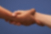 A blurred image shows one person's hand clasping another's.