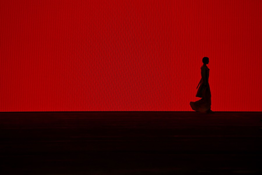A model walks, seen in silhouette against a large red screen.
