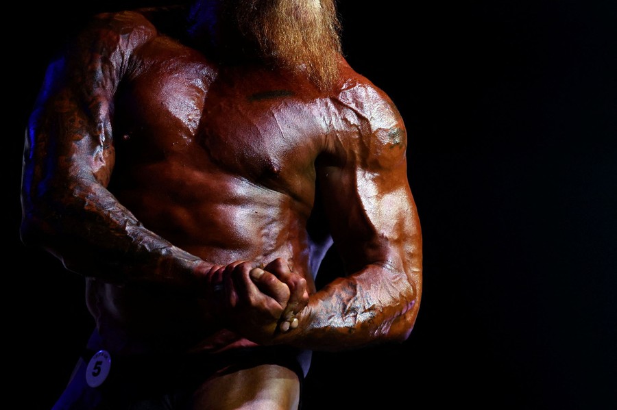 A bodybuilder flexes his arms and chest, posing.