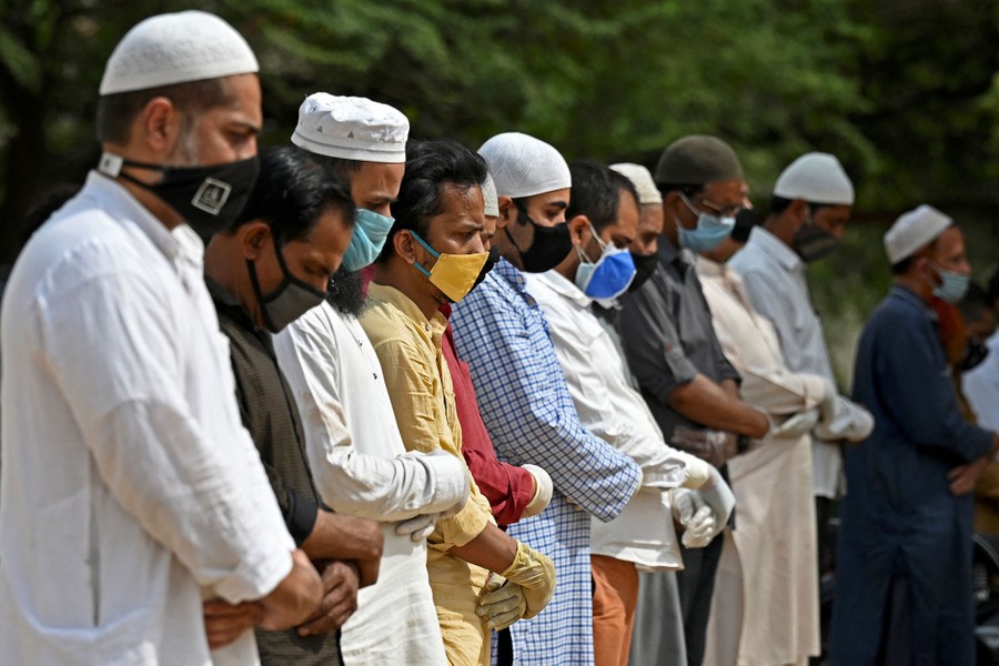About a dozen people stand side-by-side, wearing face masks, praying.