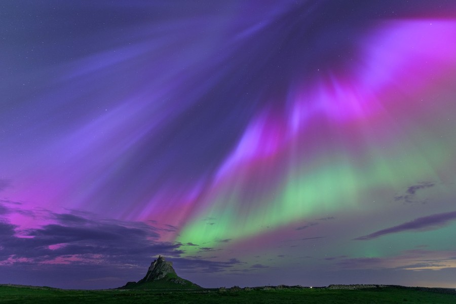 Beautiful colors appear in the sky as the northern lights glow above a castle on a hilltop.