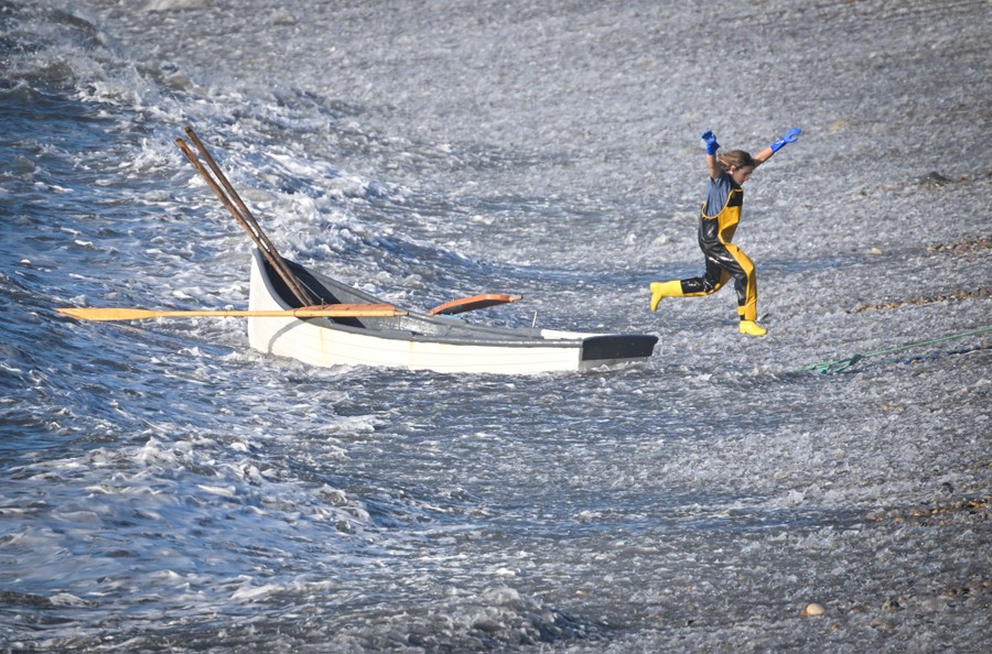A person leaps from a small boat onto the shore, as waves splash all around.