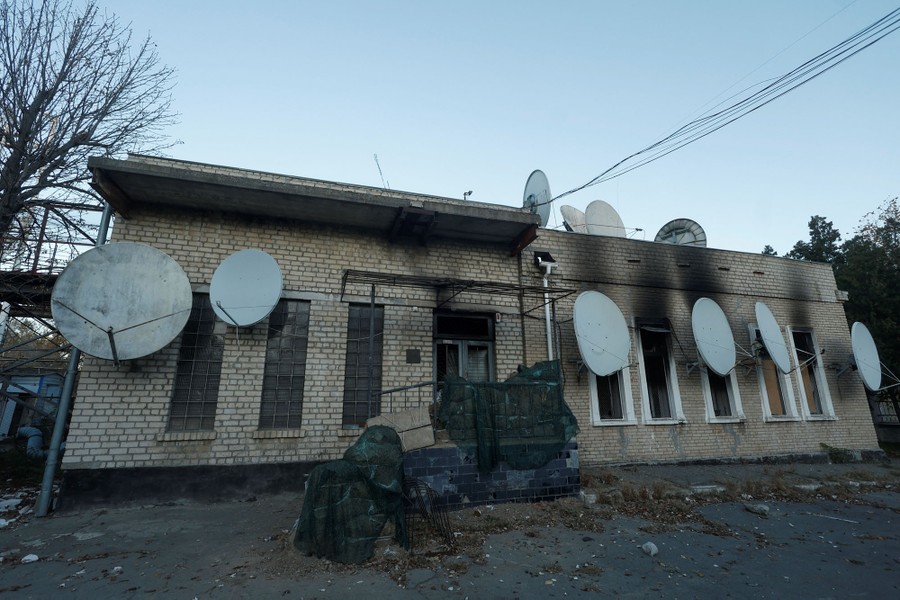 A building with numerous satellite dishes attached to it stands scorched by a fire.