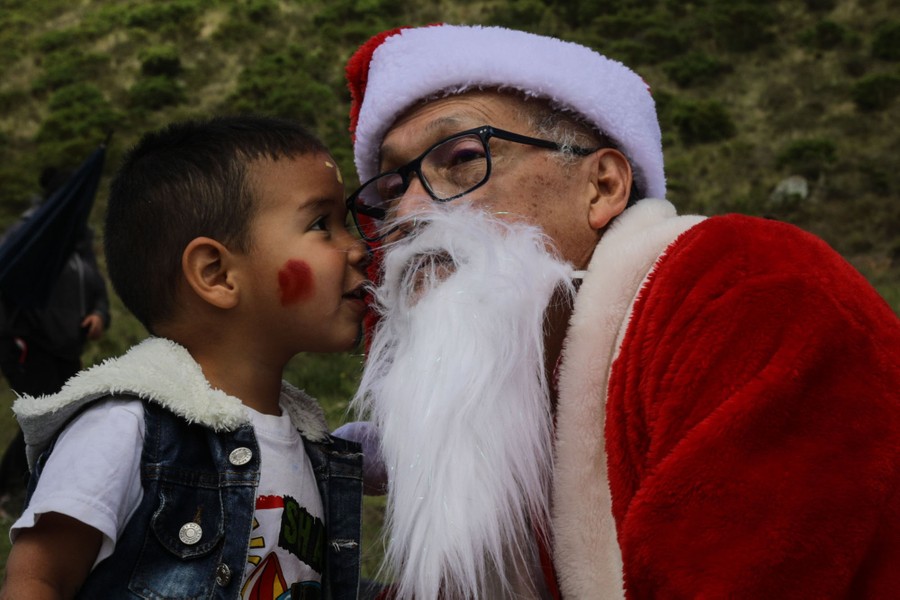 A man dressed as Santa Claus shares a moment with a child who leans in close.