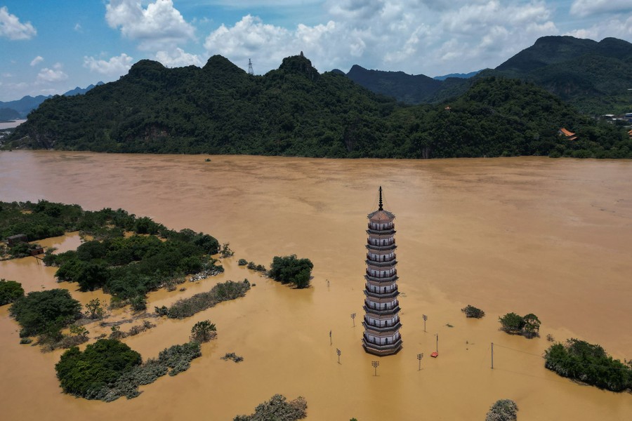 An aerial view of a tall tower stranded in a flooding river