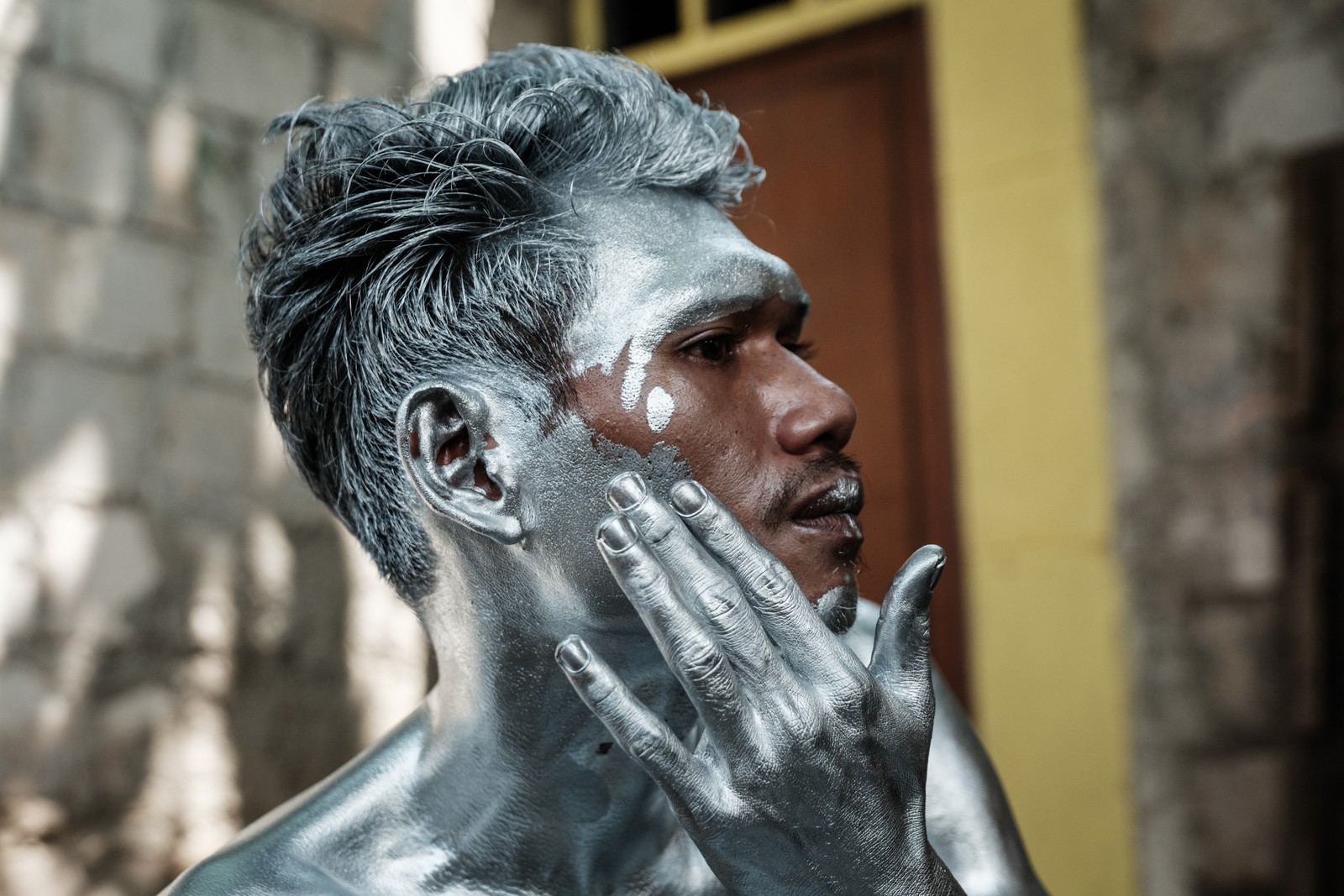 A man applies silver paint to his face and neck.