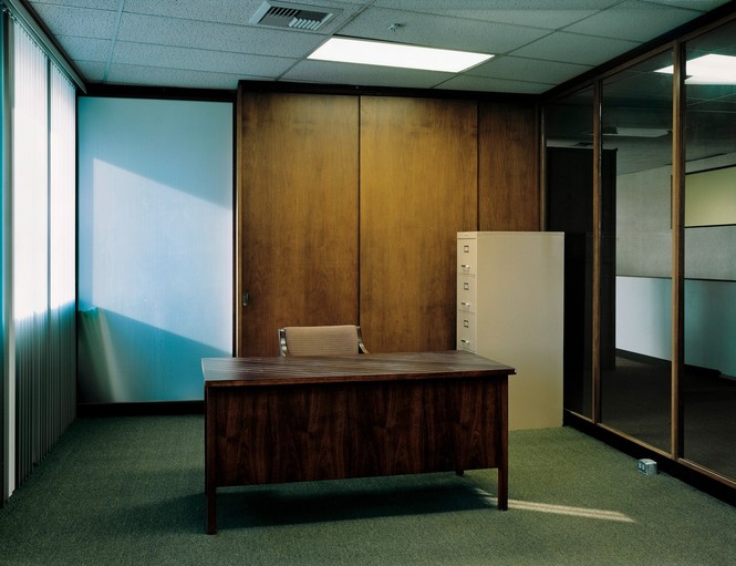 A photograph of a dreary empty office with a desk and filing cabinet