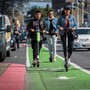 A group of people rides electric scooters from Lime and Bird in a bike lane while a cyclist passes them.