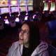 A woman wearing glasses looks up at a screen