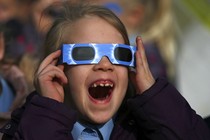 A pupil wears protective glasses as she views a partial solar eclipse from a school in Altrincham.