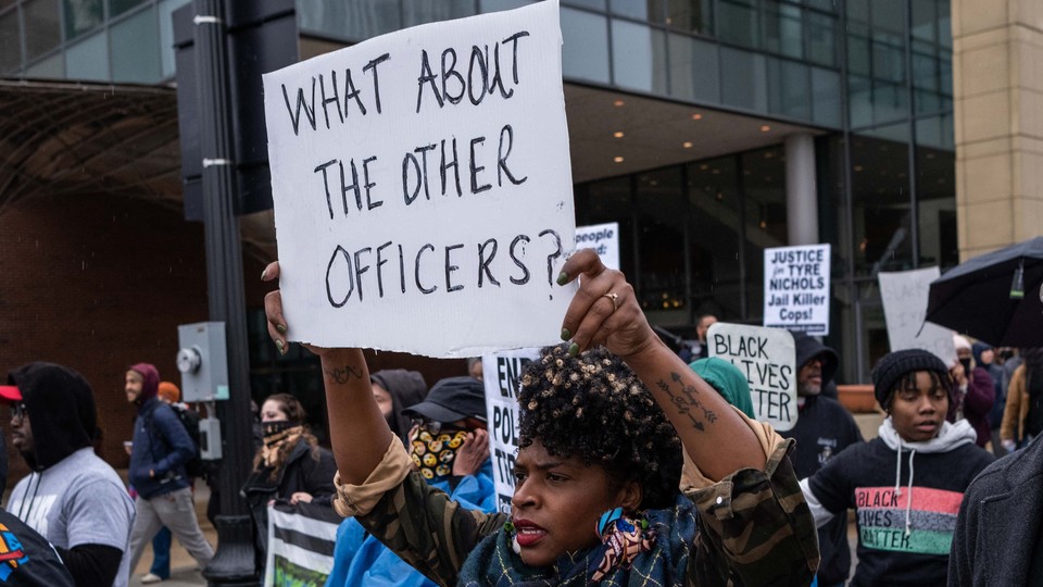 Protesters march. One holds a sign that reads, "What about the other officers?"