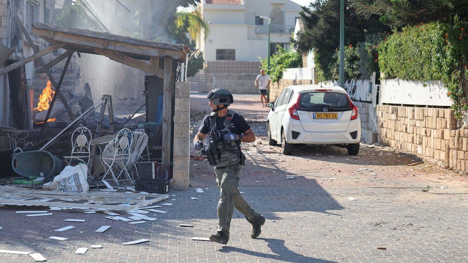 A member of the Israeli forces runs past a fire in Ashkelon following a rocket attack from the Gaza Strip.