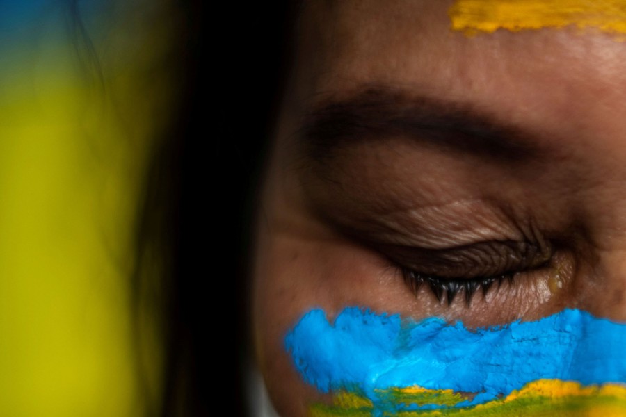 A close view of the face of a protester, wearing blue and yellow makeup.