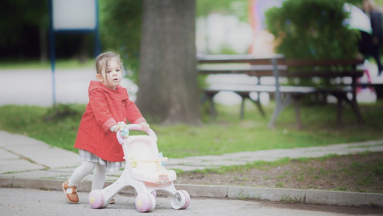 A child pushes a stroller down a street.