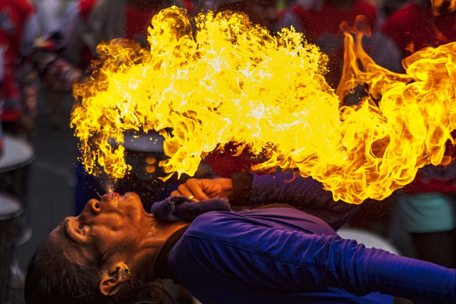 A person leans far back while spitting fuel into a large fireball above them.