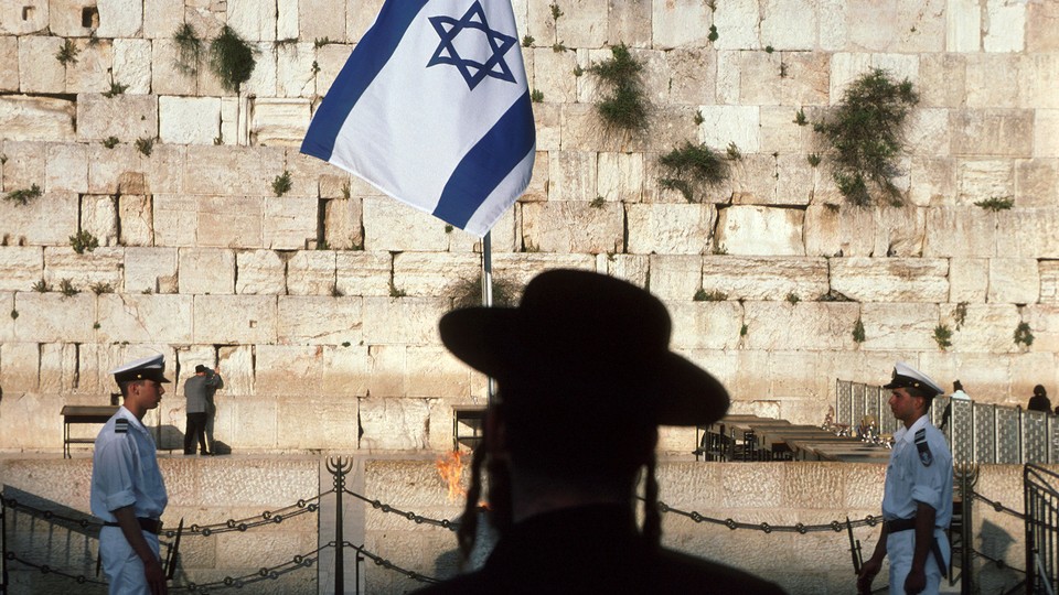 A photograph of the Wailing Wall with an Israeli flag and two guards.