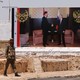 A soldier stands on a road in Syria in front of a billboard with a photo of Assad and Putin shaking hands.