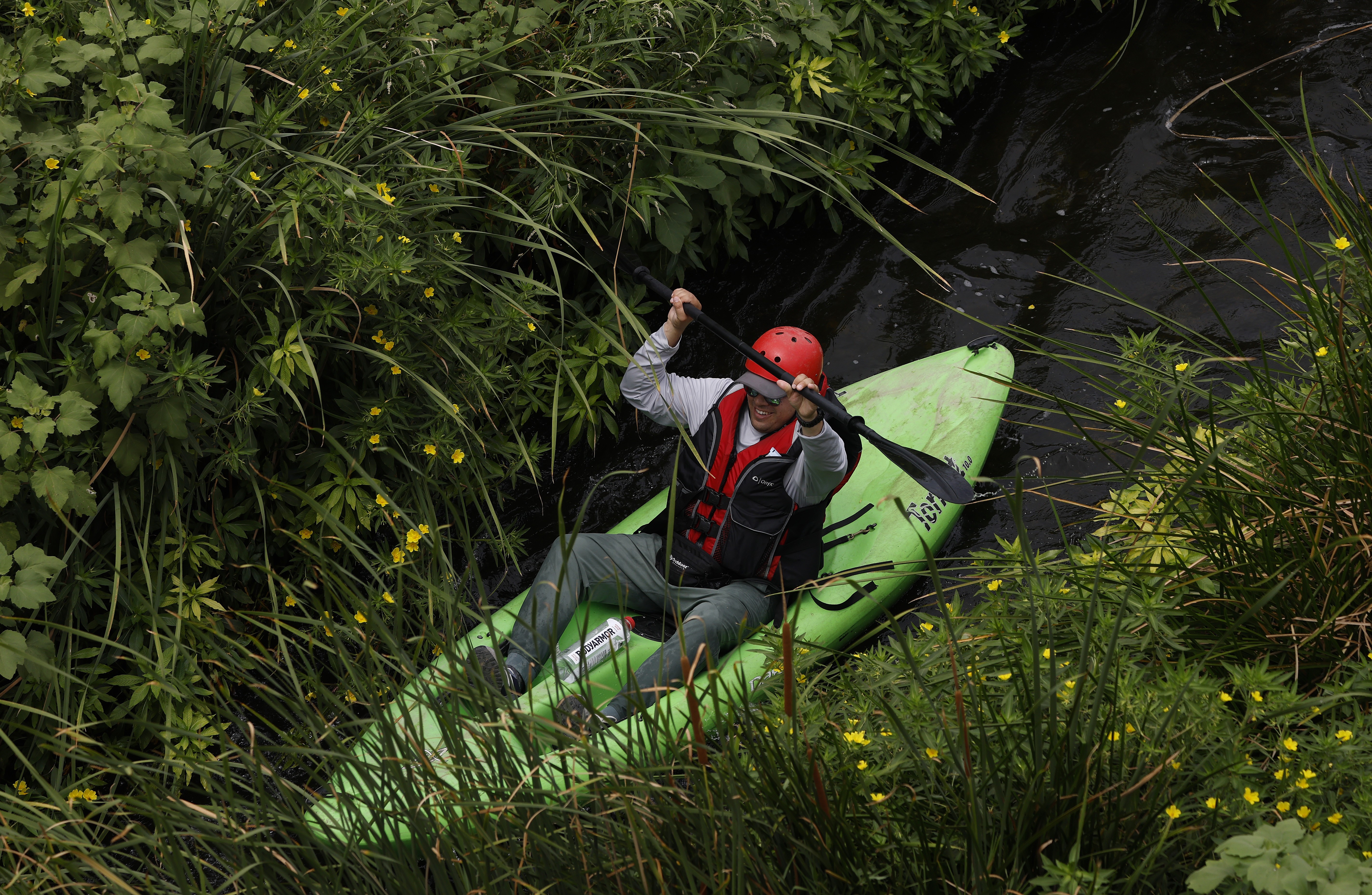 A kayaker paddles through brush.