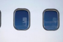 Two windows on the side of an airplane show hands holding up smartphones inside.