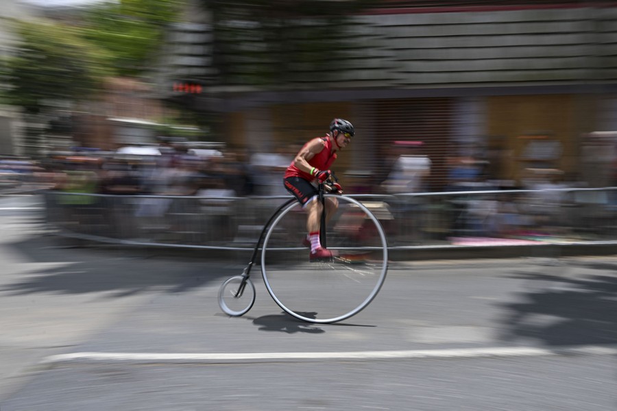 A person rides a high-wheel bicycle in a race. The bicycle has one very large wheel in front, and one very small wheel in back.