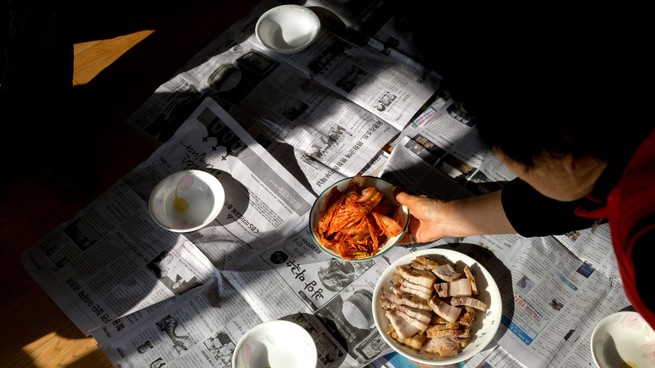 A person leans over bowls of food placed on top of newspapers