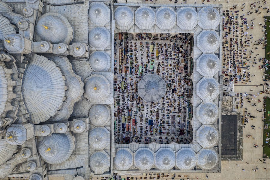 An aerial view of a mosque and courtyard filed with people lined up in prayer.