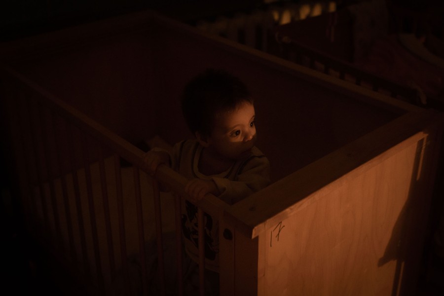 A young child stands in a crib in a dimly lit room.