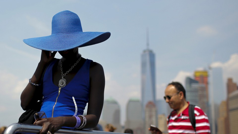 A woman in a sunhat speaks on a cellphone in front a city skyline.