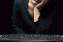 A woman rests her face on her hand while sitting in front of a computer keyboard.