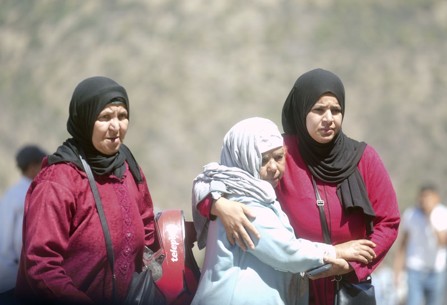 Three women stand together, giving comfort to one another.