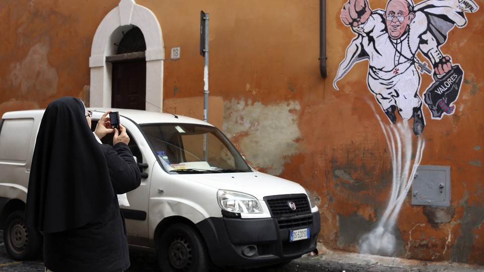 A nun takes a picture of a drawing of Pope Francis depicting him as a superhero on a wall near the Vatican.