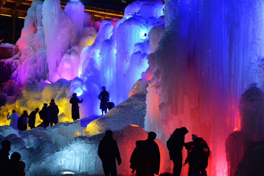 Dozens of people walk near large illuminated ice sculptures.