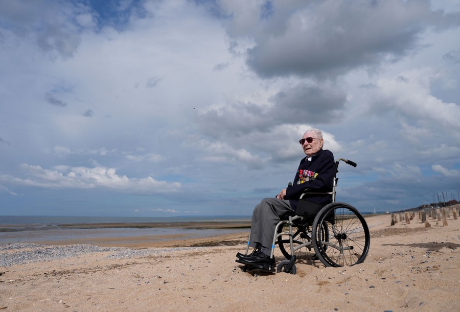 An elderly veteran in a wheelchair sits on a beach.