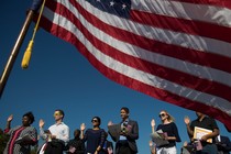 Framed by an American flag, immigrants raise their right hands and take the oath of allegiance during a naturalization ceremony.