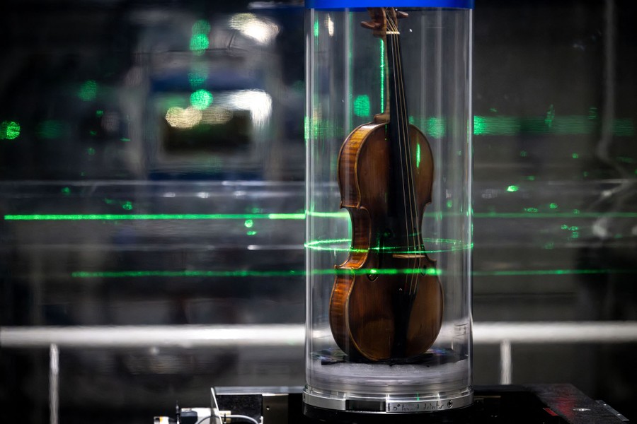 A violin sits inside a clear tube as green laser lights illuminate parts of it.