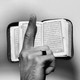A photograph of a raised finger in front of a Quran