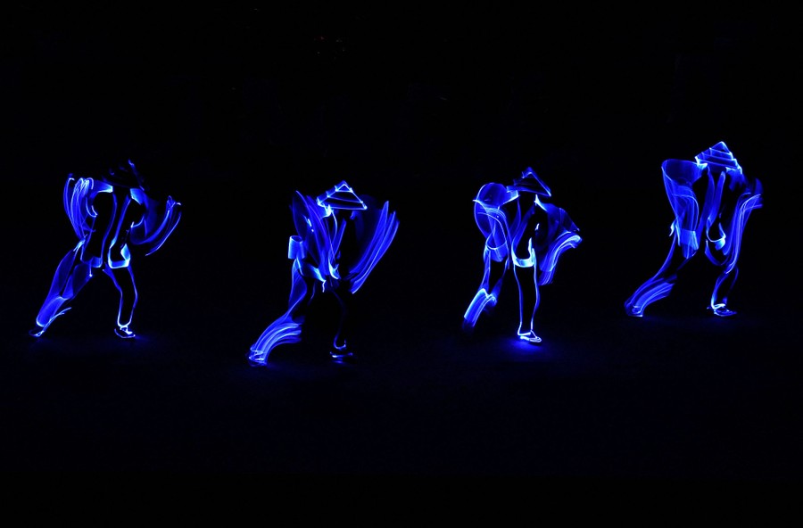 Four dancers perform in the dark, wearing illuminated clothing.