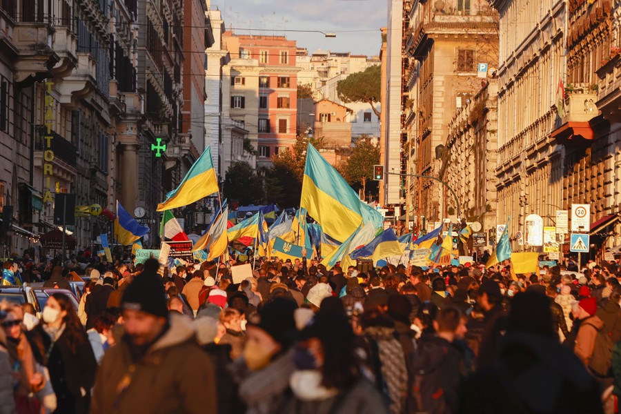 A large crowd of people carrying Ukrainian flags marches in a city street.