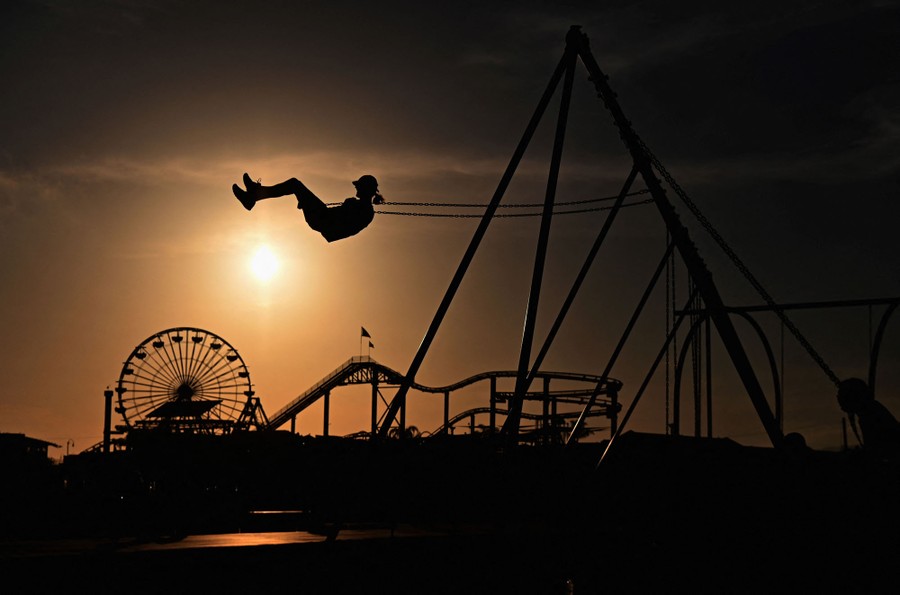 A person swings high on a swing set with an amusement park visible in the background.