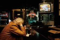 An old man holds his head watching the TV at a bar alone