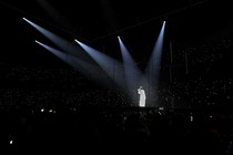 Suga sings in a dark arena, with five spotlights on him.