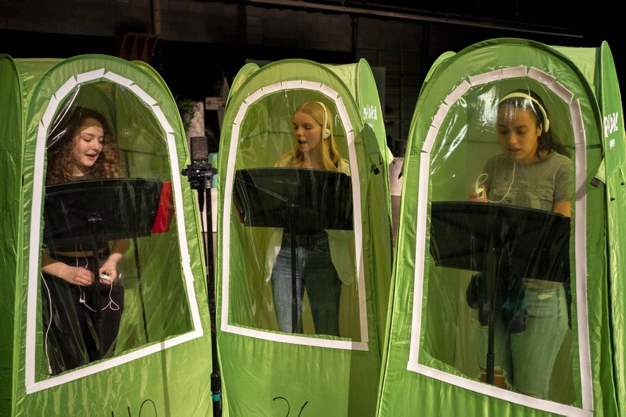 Three students stand in separate small tents, singing during a choir class.
