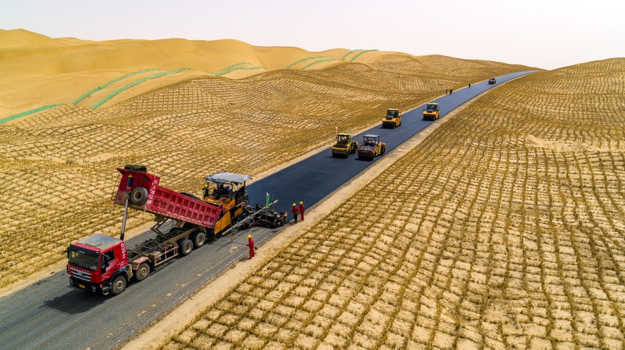 Workers build a highway in a broad desert.