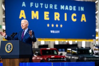 Joe Biden at a podium, with electric cars in the background behind him
